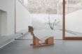 A wooden chaise lounge chair in a minimalistic room
