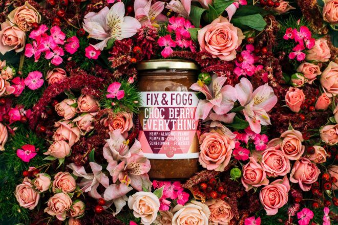 A jar of Fix and Fogg nut butter surrounded by different color pink and red flowers
