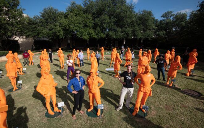 Women standing beside sculptures of themselves that were 3D print in an orange color