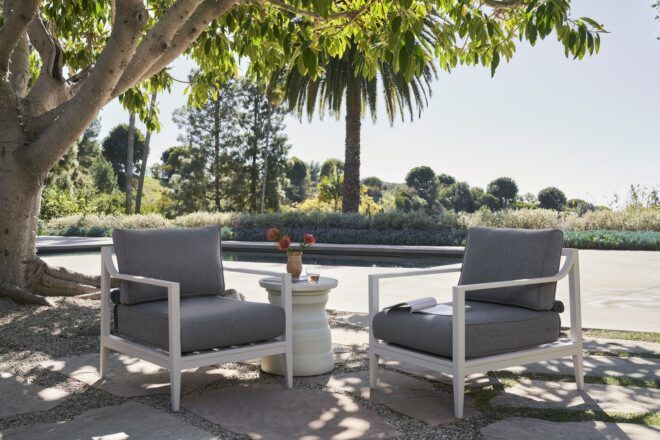 Two grey chairs facing each other with the background of a pool and trees