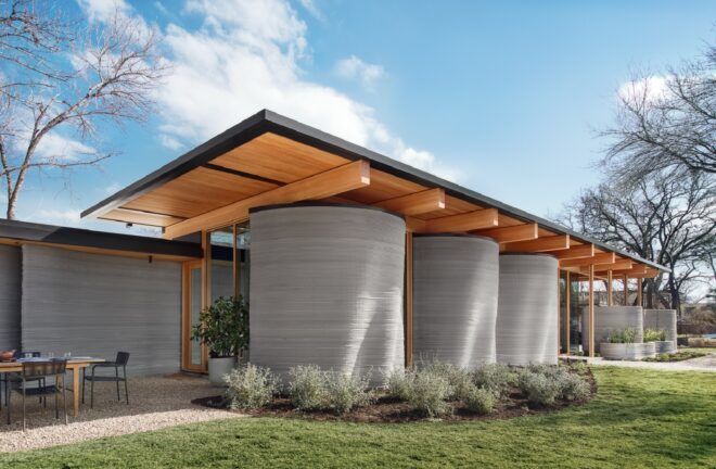 The House Zero has three column-like grey structures that holds up a wooden awning connecting to the main building