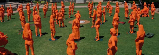 Orange 3D printed sculptures of women trailblazers on a grass field