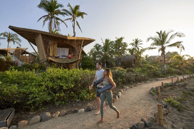A person walking on a sandy path by a bamboo structure.