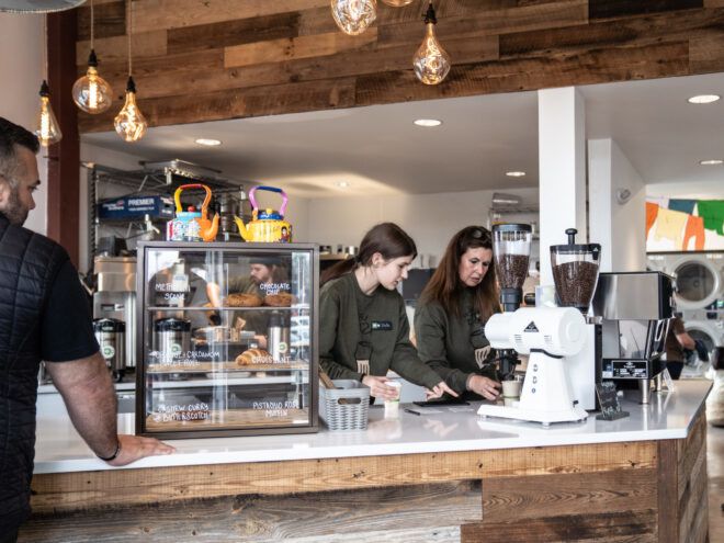 Cafe counter with pastries in glass display case and two baristas preparing coffee