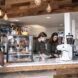 Cafe counter with pastries in glass display case and two baristas preparing coffee