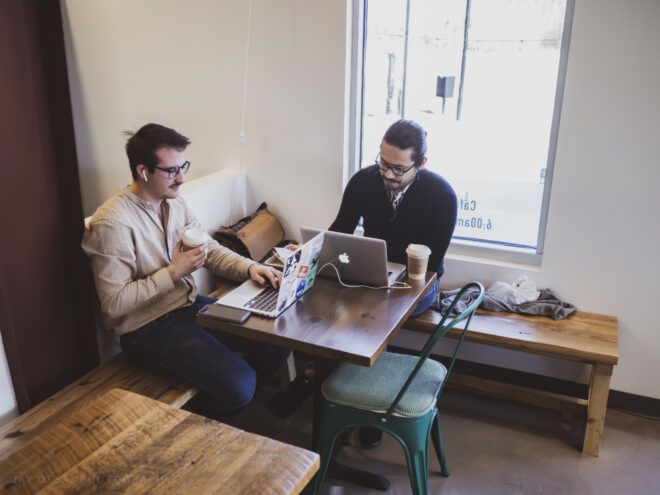 Two men sitting on a corner table of the laundry lounge, working on their laptops and having coffee