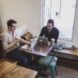 Two men sitting on a corner table of the laundry lounge, working on their laptops and having coffee