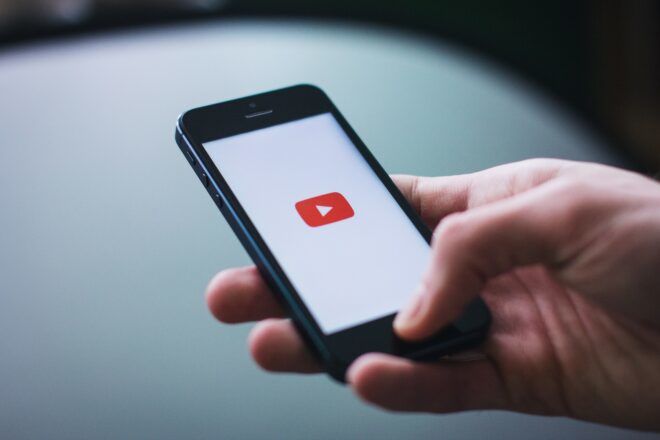 A hand holding a phone with the YouTube logo on it, which is a red rectangle with a triangle within it