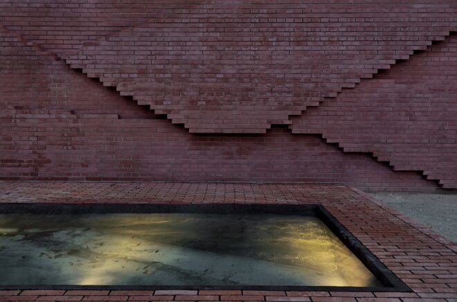 A reddish brown wall with a pool of water in front of it