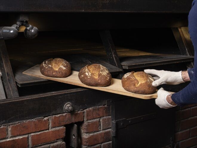 Three loaves of bread lined on a wooden paddle