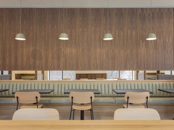 A wood wall contains plush striped seating with wooden chairs on the other side of it