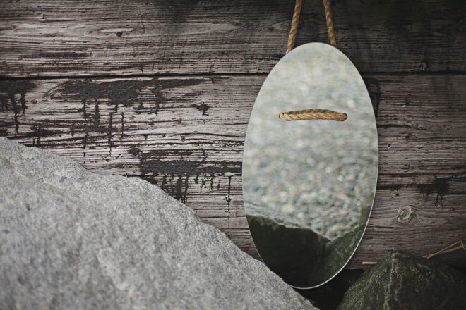 A mirror with a wood grain string to hang it up lays on a wooden floor