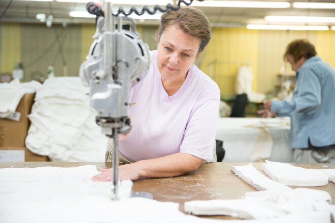 A woman wearing a light pink shirt sews together white fabric