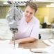 A woman wearing a light pink shirt sews together white fabric