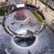 A large sculpture in the shape of an O stands on a circular platform in the middle of a town's square