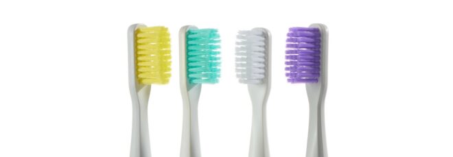 Four toothbrush heads in varying color bristles, from left to right: yellow, teal, white and purple