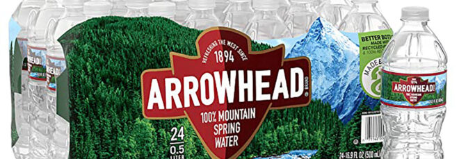 A case of plastic water bottles with the label Arrowhead on it. There is also a single plastic water bottle standing beside it
