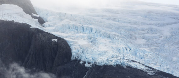 A blue glacial melt beside some dark colored mountain