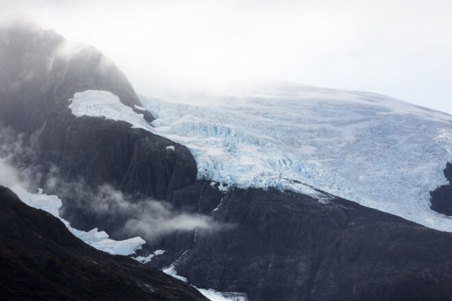 A blue glacial melt beside some dark colored mountain