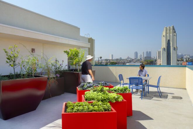 Roof deck with bright planters and seating for residents. In the background, the city of LA is visible