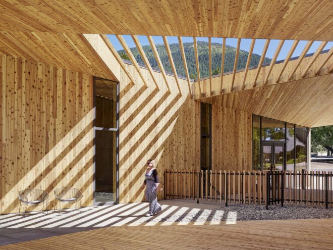 A wooden open pavilion with a cross-section roof that allows sunlight through