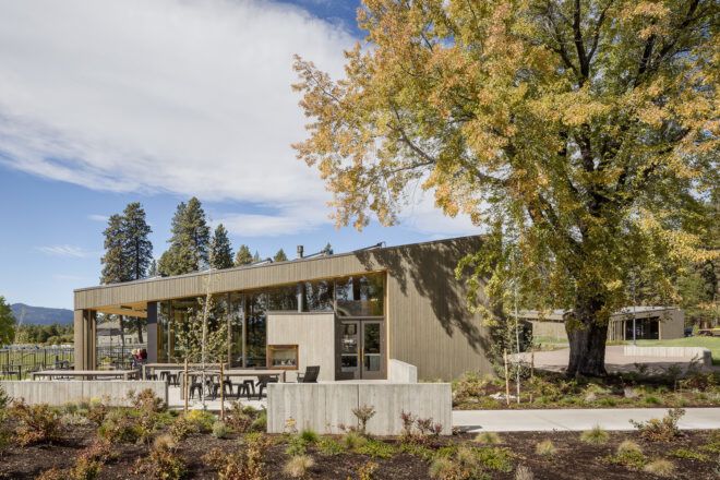 A slanted roof lakeside ranch surrounded by trees and within distance of a mountain landscape