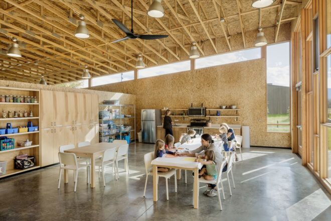 A seating area of the lakeside ranch has wooden interiors and wooden tables where a mom and her children are playing