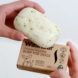 A hand holding a bar of soap and the cardboard WashBar packaging with the other hand