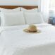 A white bed with four white pillows and white covers with a tan wide-brimmed hat sitting on it