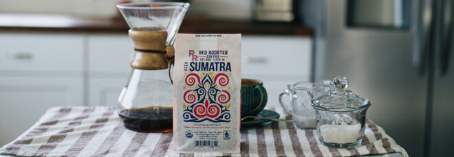 A kitchen scene. At the table is a Red Rooster Coffee bag with a coffee pour over set