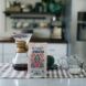 A kitchen scene. At the table is a Red Rooster Coffee bag with a coffee pour over set