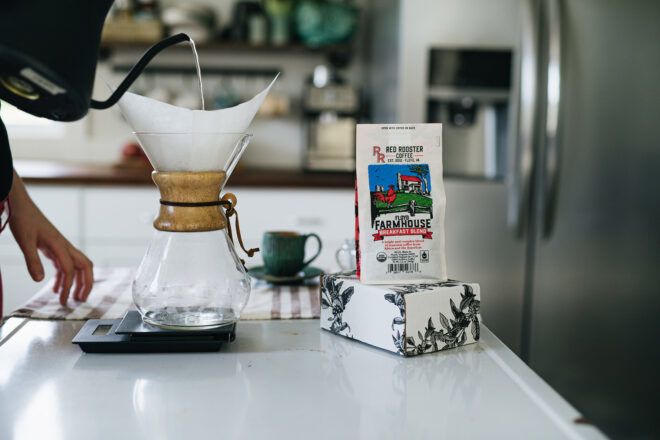 A person pouring into a pour over coffee pot with a coffee bag next to it