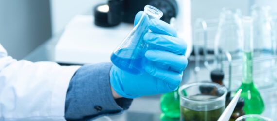 A gloved hand holding a beaker to illustrate PFAS.