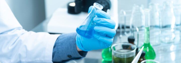 A gloved hand holding a beaker to illustrate PFAS.