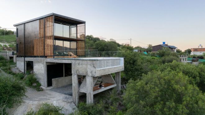 A multistory house that has a bottom concrete and top wood slates surrounded by trees