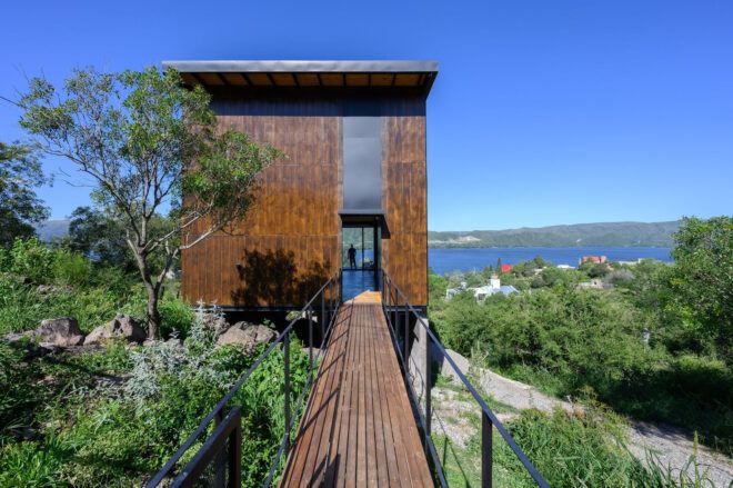 A wooden platform connects to a wooden house that overlooks a water horizon