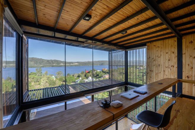 A long wooden desk that connects from one side to another overlooks a water and hill horizon