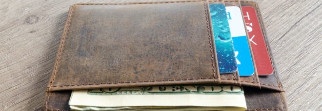 A brown leather wallet filled with cards in its pockets and cash bills sticking out in another pocket