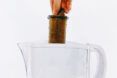 A person holding a wooden object into a glass pitcher