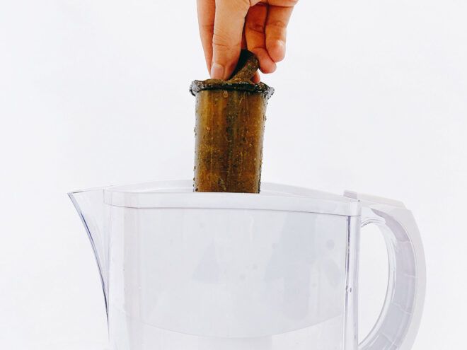 A person holding a wooden object into a glass pitcher
