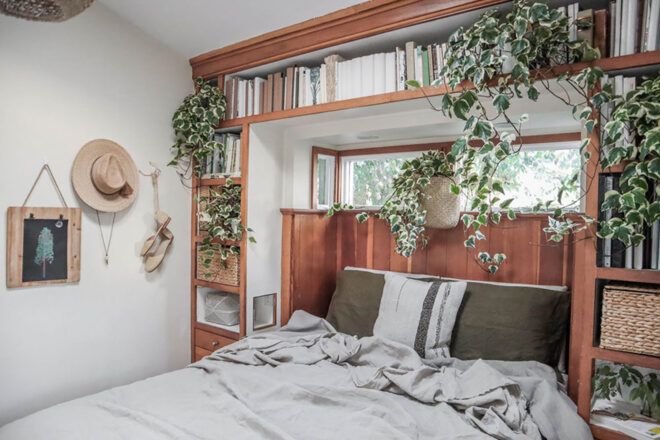 A bed with a bookshelf lined around and above it covered in plants