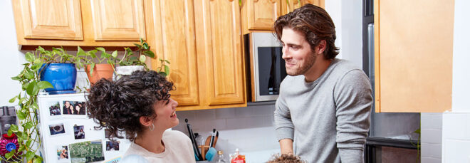 A man and a woman facing each other talking in a kitchen