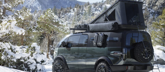 A Canoo pickup truck exterior with a camper on the top parked in a snowy forest