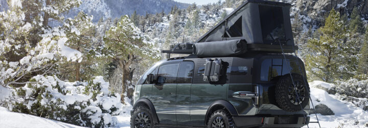 A Canoo pickup truck exterior with a camper on the top parked in a snowy forest