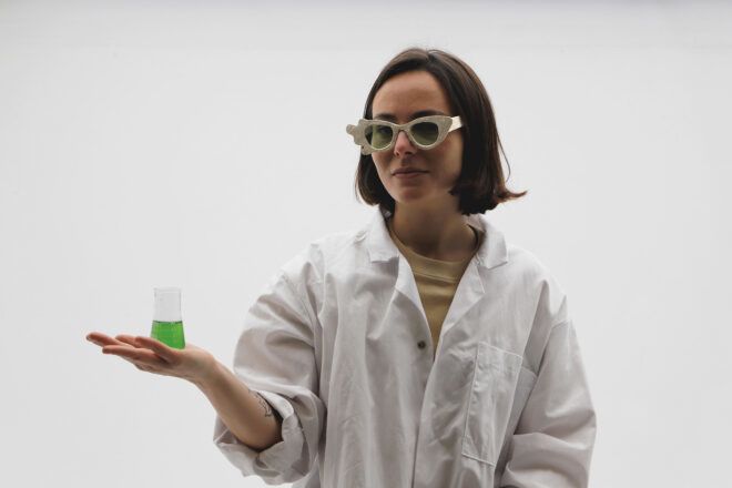 A woman with above-the-shoulder hair with a glass vial filled with a green liquid balanced on her palm