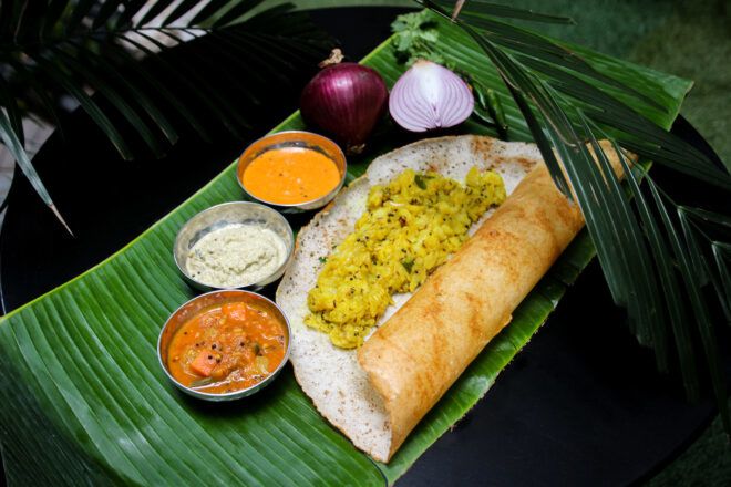 A dosa surrounded by different dipping sauces on a banana leaf
