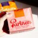 A hand holding a pink coffee box that reads Partners Coffee