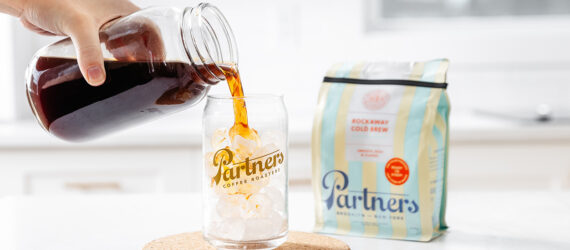 A hand pouring a cup of coffee into a cup filled with ice