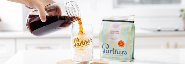A hand pouring a cup of coffee into a cup filled with ice