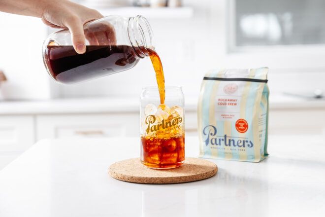 A hand pouring a cup of coffee into a cup filled with ice